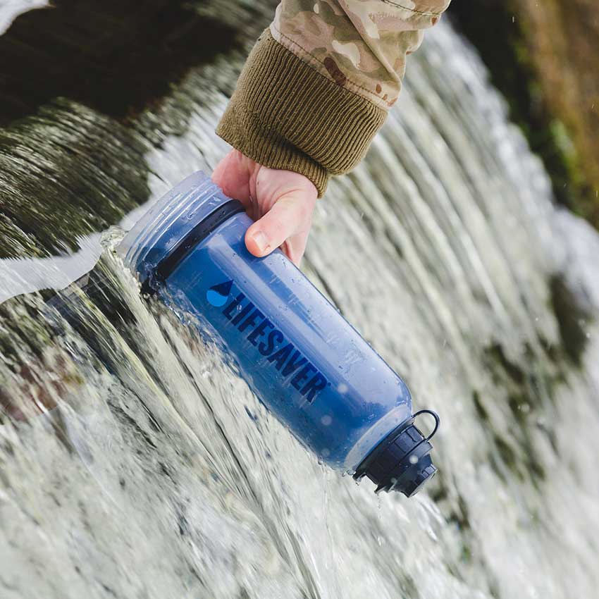 Person filling LifeSaver water bottle with water from waterfall