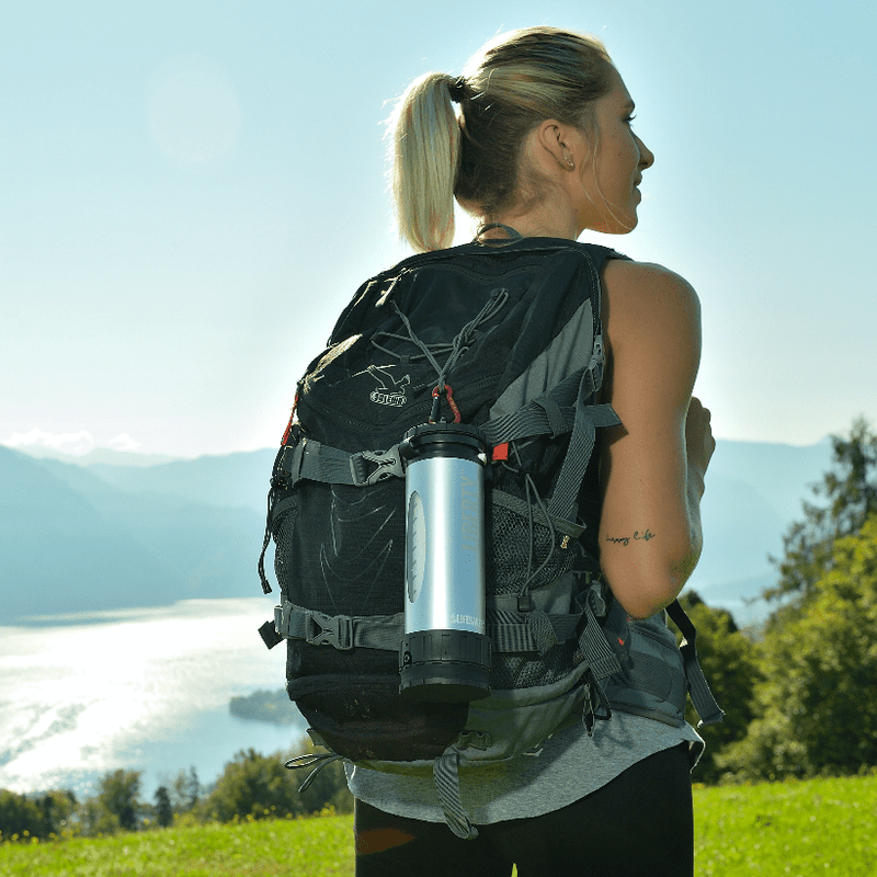 Load image into Gallery viewer, Athletic woman in outdoor gear, with a LifeSaver Liberty attached to her outdoor rucksack, by a lake in Austria.
