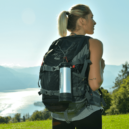 Athletic woman in outdoor gear, with a LifeSaver Liberty attached to her outdoor rucksack, by a lake in Austria.