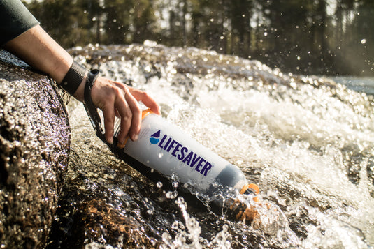 A LifeSaver Bottle water filter bottle being filled at some rapids in a river