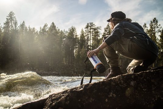 A hiker crouching beside a fast moving river with a LifeSaver Bottle